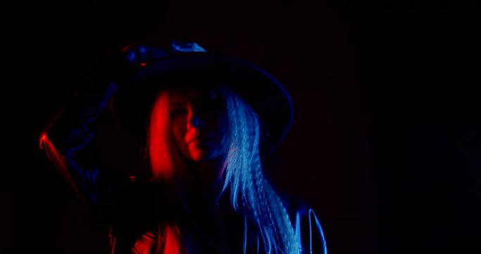 portrait of a blonde with long hair on a black background. she puts on her hat. blue and red light. dark key