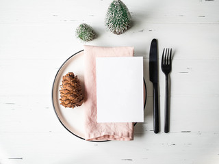 Obraz na płótnie Canvas Rustic table setting for christmas or new year. White plate, pink napkin, pine cone and appliances on white wood table. Top view.
