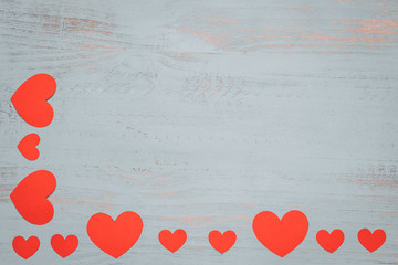 Paper hearts and a white present with red ribbon on a light painted wooden background. Top side angle view, flat lay. Valentines day concept. Copyspace.