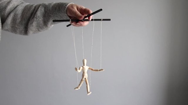 Manipulator female hand manipulates a wooden doll on a gray background. Management or suppression concept