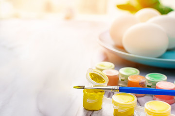 Easter concept - colorful paint with a brush and a blue plate with eggs for traditional painting eggs on a marble table on a sunny morning