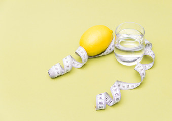 Measuring tape with glass of water and lemon on yellow background. Diet concept.Free copy space.