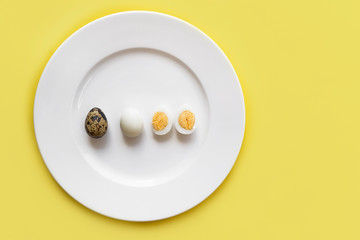 Group, set of peeled and unpeeled small organic quail eggs, whole cut in halves, halved boiled versus raw on a white plate on yellow background. Top view from above. Before cooking and after. Egg yolk
