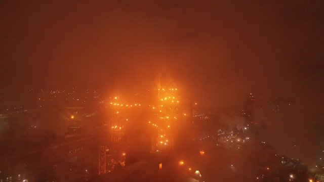 Aerial view of metallurgical plant blast furnace at night with smokestacks and fire blazing out of the pipe. Industrial panoramic landmark with blast furnance of metallurgical production. 