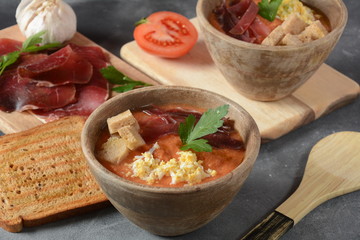 Traditional Spanish andalusian tomato cream soup Salmorejo served with egg, ham jamon, bread in woooden bowl. Summer cold soup concept