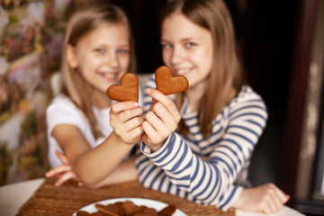 Charming, funny and laughing girls on a blurry background are holding heart-shaped cookies on an outstretched arm, two hearts, close-up