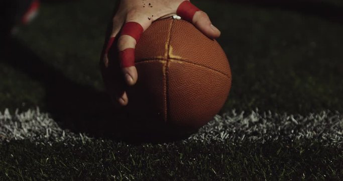 EXTREME CU of Caucasian male American football player holding a ball on grass to start game. Slow motion 60 fps 4K RAW edit footage
