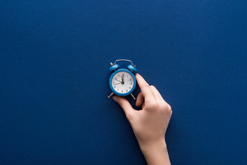 cropped view of woman holding small alarm clock on blue background