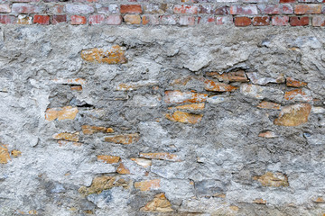 The texture of a rough stone and brick wall with peeled plaster