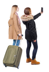 Back view of two woman in winter jacket traveling with suitcas.