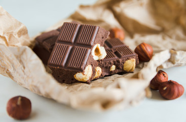 Pieces of milk chocolate with hazelnuts randomly lie on beige mashed craft paper