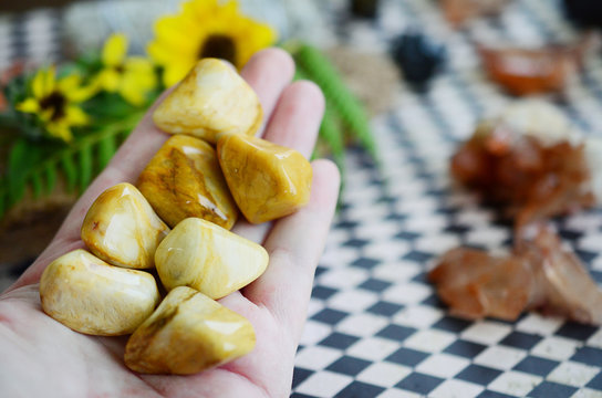 Woman's hand holding yellow jasper healing crystals. Tumbled yellow crystals, natural lighting and lush color. Intricate yellow swirls on beautiful jasper, witches healing stone. Wiccan alter magic