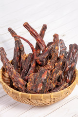 Straw bowl full of dried oxtails. Could be used in exotic cuisine or as natural chew treats for big dogs. Dehydrated foods. Indoors, white background, copy space.