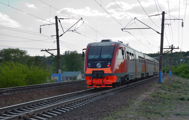 Fototapeta na wymiar New commuter train, colored in red and grey, goes by rail. A diesel-electric rail bus rides by suburb at dusk