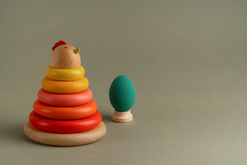 Handmade wooden eco-friendly toy chicken pyramid and wooden painted eggs on green paper background. Happy Easter concept. Educational and educational toys for children