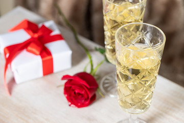 Two Champagne glasses, red rose flower  and gift box with bow on the table .Romantic date concept or Saint Valentines day celebration.