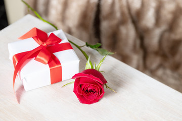 Red rose and white gift box with red ribbon bow on wooden background. Giving present concept.