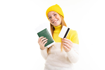 Happy teenager girl with red hair, hoody and hat holds passport and credit card isolated on white background