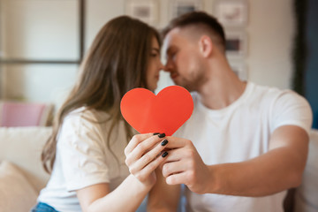 young couple kissing on the sofa, both holding big red paper heard on saint valentine's day, happy unniversary