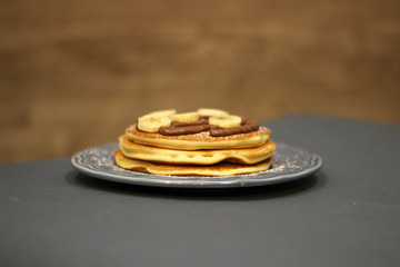 pancakes with chocolate and banana on blue plate and wooden and dark background