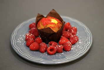 raspberry muffin on a plate with raspberries on dark background