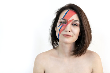 red and blue lightning bolt on her beautiful face. Beautiful girl with original make-up on a white...