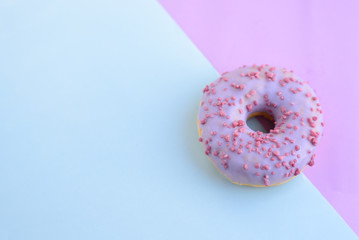 Delicious bright juicy purple one sprinkled donut for a sweet tooth on a purple and blue background. Close-up top view, unhealthy baked goods with sugar. Free space for text