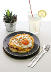 salted pancakes with bacon, cheddar cheese and egg on a gray plate with cutlery, fork and knife, lemonade with a slice of lemon and ice, and a vase with a cactus