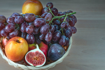 Naklejka na ściany i meble figs, nectarine and red grapes in a straw basket on a wooden background