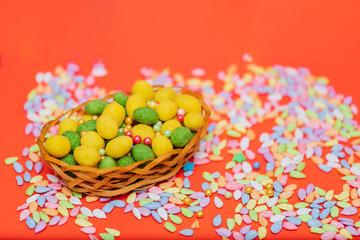 Easter composition, green and yellow dragee in a basket on a red background. Egg, nuts in the glaze, sunflower seeds in colored glaze. Flat lay.