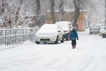 Fototapeta premium child walking in the snow next to parked cars