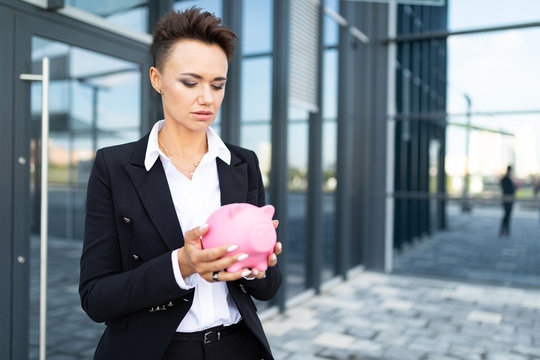 Elegant young beautiful businesswoman holds a piggy bank on the background of the entrance of a business center building