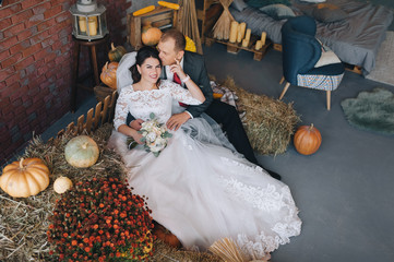 Stylish groom and beautiful bride in a white dress with a bouquet are sitting on the hay in the...