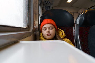 Teenager girl in a yellow jacket sitting in a suburban train and slipping. Vacation and daily journey from school home