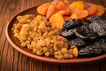 Assortment of dried fruits and raisins and apricots with plums in a plate on a wooden background