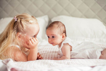 Young beautiful mother holds a baby. Little sister kisses her little sister. Baby. Children bedroom.