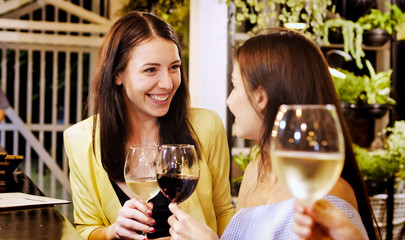 Two beautiful girls ringing glasses with drinks at the bar.