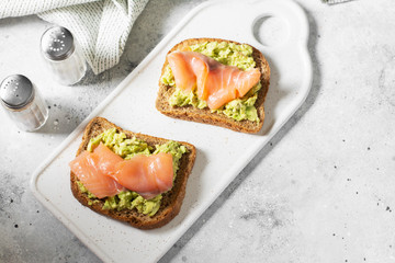 Bruschetta with avocado and salmon on a white ceramic plate on a light gray kitchen table. Toasted bread with avocado and red fish. The concept is helpful and a delicious Breakfast