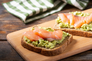 Bruschetta with avocado and salmon on a wooden Board on a brown wooden table. Toasted bread with avocado and red fish. The concept is useful and delicious Breakfast