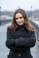 A brunette girl in a black coat is walking on a cold winter day without snow. Portrait of a girl.