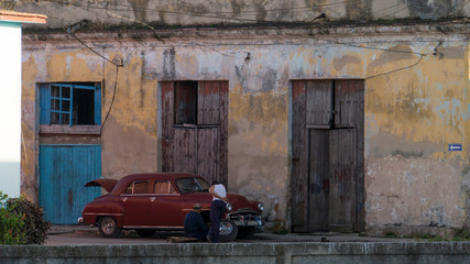 two cuban men repairing a cuban classic car in front of an old house