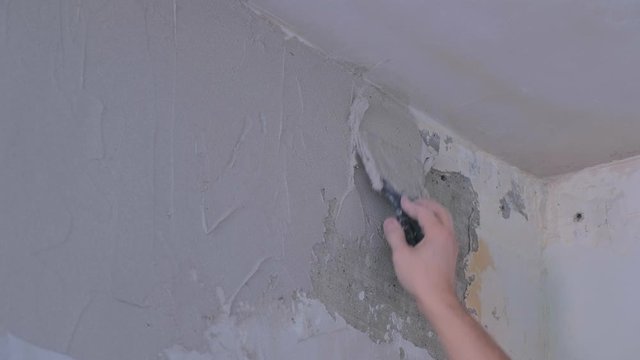 Plasterer man is spackling with putty plaster aligning wall with trowel, hands closeup. Finishing construction renovation works. Worker builder making overhaul applying plaster on wall using spatula.