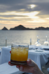 restaurant table setting close up with margarita cocktail held up in foreground and sunset in background Baja Mexico