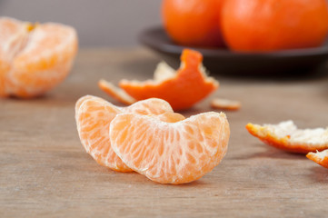 Slices of ripe mandarin(tangerine) on a wooden table against the background of whole tangerines and tangerine skins.