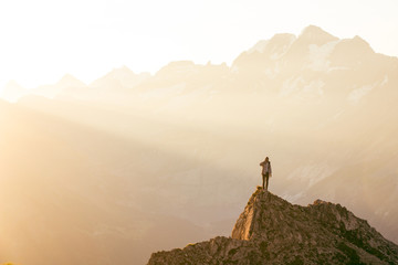  a man stands on a rock, shrouded in the morning sun, surrounded by mountains