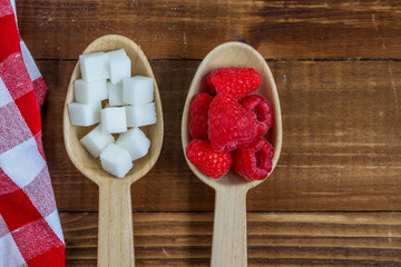 Healthy raspberries and uhealthy sugar in wooden spoons on wooden background