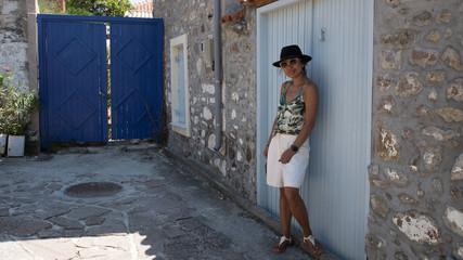 Asian Woman in sunglasses and hat standing in front of traditional Greek house