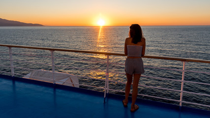 Asian teen in tube top standing on deck of ferry looking at sunset