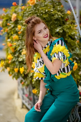 A young beautiful girl of model appearance in a bright colored jumpsuit on the street.