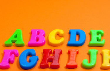 Plastic color letters on a bright contrasting orange background, multicolored alphabet with copy space